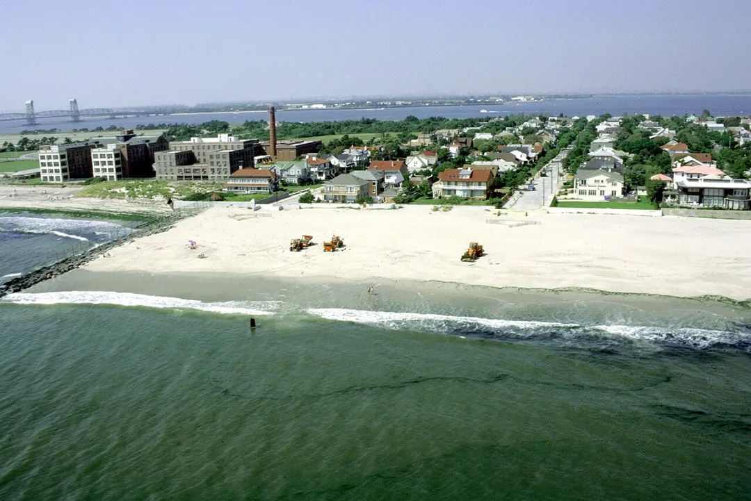 Aerial view of the beach area of Rockaway Park neighborhood, Queens, New York. The photograph appears to be taken from directly off the end of Beach 148th Street in the Neponsit area, next to Jacob Riis Park. The U.S. Army Corps of Engineers is working to replenish the sand on the beach.  en:Marine Parkway-Gil Hodges Memorial Bridge in background left.