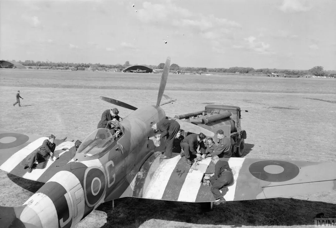 Royal Air Force ground crew refuel and re-arm Hawker Tempest Mark V 'JF-G' of No. 3 Squadron RAF by the grass North-South runway at Newchurch, Kent (UK). On the far side of the runway is the dispersal area of No. 56 Squadron RAF.