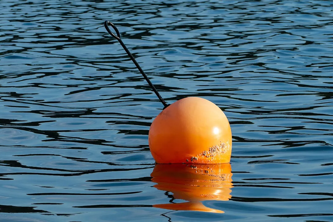 An orange mooring buoy in the water of Hanneviken, a part of Trommekilen and Brojorden, lit by the setting sun. Norrkila, Lysekil Municipality, Sweden.