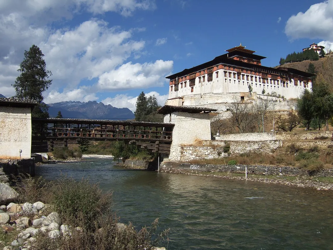 Rinpung Dzong(རིན་སྤུང་རྫོང) in Paro Bhutan with a cantilever bridge over the Paro Chu river in the foreground and the National Museum of Bhutan (Ta Dzong) on the hill in the background.