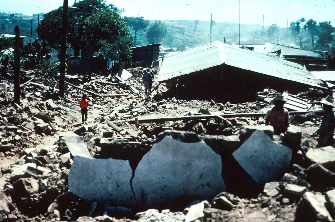"Guatemala Earthquake 1976. Typical street view in Patzicia, showing adobe block rubble which is all that remains of the houses that formerly lined this street. The adobe block buildings had very little resistance to horizontal forces and most of them were completely destroyed. Collapse of the heavy adobe walls, roof tiles and beams caused most of the casualties. Many of the adobe blocks are still intact but the mortar between the blocks failed during the seismic shaking. 1976. Slide 43, U.S. Geological Survey Open-File Report 77-165."
Note: this was from the earthquake of 4 February, 1976.