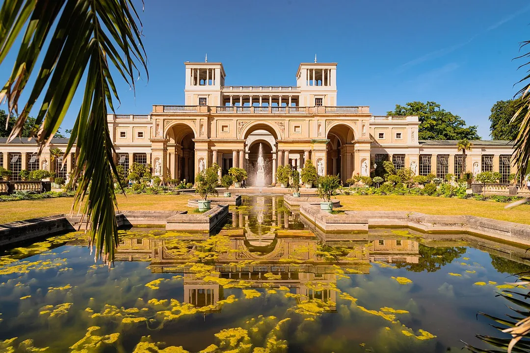 The Orangery palace with fountain in front of it. The palace is partially mirrored on the water surface of the fountain.