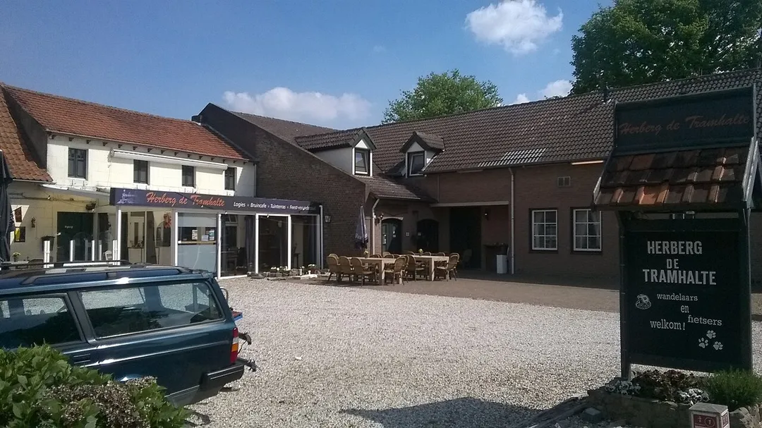 Horecagelegenheid op Kasteel Ter Borchstraat 3 te Roosteren. Tussen 1922 en 1937 halte van de tramlijn Roermond - Echt - Born - Sittard. Halte lag ook aan de zijtak van de lijn naar Maaseik. Op de gevel van de serre staat geschreven: Herberg De Tramhalte en verder: Logies Bruincafe Tuinterras Feest-vergaderzaal. Links is de achterkant van een blauwe Volvo 245 te zien. Foto genomen van de Kasteel Ter Borchstraat in noordoostelijke richting.