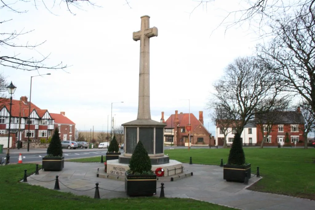 Photo of Ryhope village Green, facing East showing the World War I war memorial. In the background a wooden "Ryhope Village" sign can be seen.