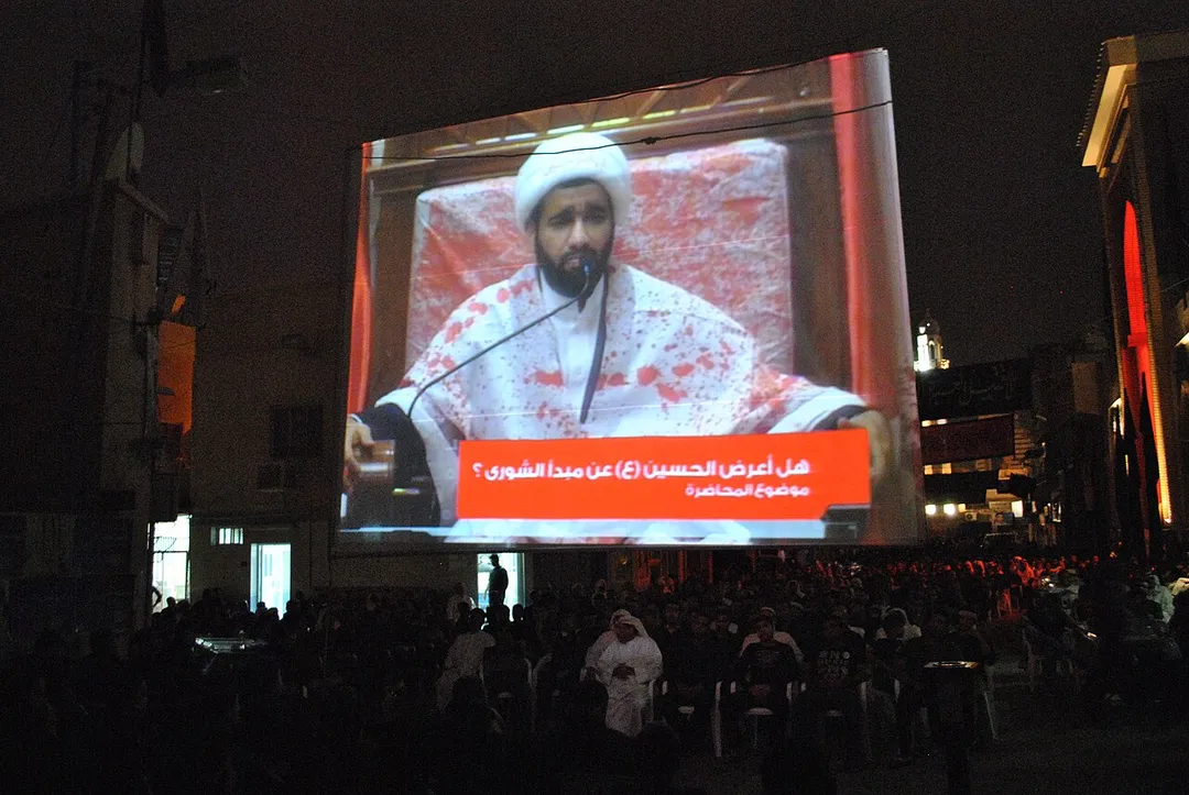 A projecter displaying Bahraini Shia cleric Hassan al-A'ali for listeners outside of Sanabis Matam. The cleric is wearing a white shroud with red stains representing the readiness to sacrifise self.