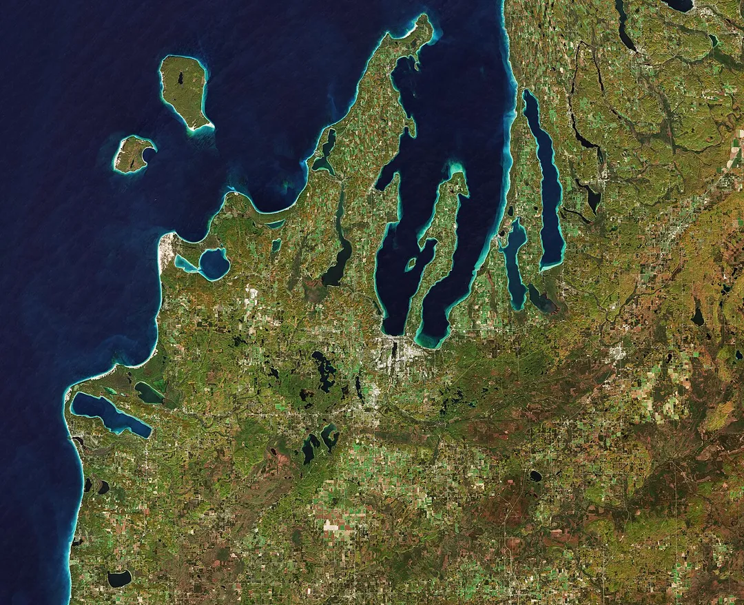 The Copernicus Sentinel-2 mission takes us over the Leelanau Peninsula on the northwest coast of Northern Michigan, US.The region is shaped by rolling hills, large inland lakes shaped by glaciers around 20 000 years ago which form the basis for great farmland. The body of water that surrounds the peninsula is Lake Michigan, one of the five Great Lakes of North America and the only one located entirely within the US.In the image, the bright turquoise in the water shows sediments, algae and chlorophyll in the shallower waters along the shore. The greener colours visible in Lake Leelanau to the north, Platte Lake to the west, and several inland bodies of water are due to a combination of a high chlorophyll and plant content.The Sleeping Bear Dunes Lakeshore extend for around 55 km along the coast of the peninsula, and is visible in light brown. The name comes from an Ojibwa legend in which a mother bear and her two cubs swim across the lake trying to escape a forest fire. The two cubs are said to have disappeared in the process, and the mother bear waited for weeks for them to re-surface before finally falling asleep and never waking. Touched by her suffering, a powerful spirit is said to have covered her with sand, and raised the two cubs above the water, creating the North and South Manitou islands, visible north of the peninsula.A more realistic explanation of the creation of the Sleeping Bear Dunes is geology. During the last Ice Age, glaciers spread southwards from Canada burying this area under sheets of ice. During the process, piles of sand and rock were deposited in the area. When the ice retreated and melted, it left the hilly terrain that exists along the lake today. The area is popular for hiking and climbing.This image, which was captured on 18 October 2018, is also featured on the Earth from Space video programme.