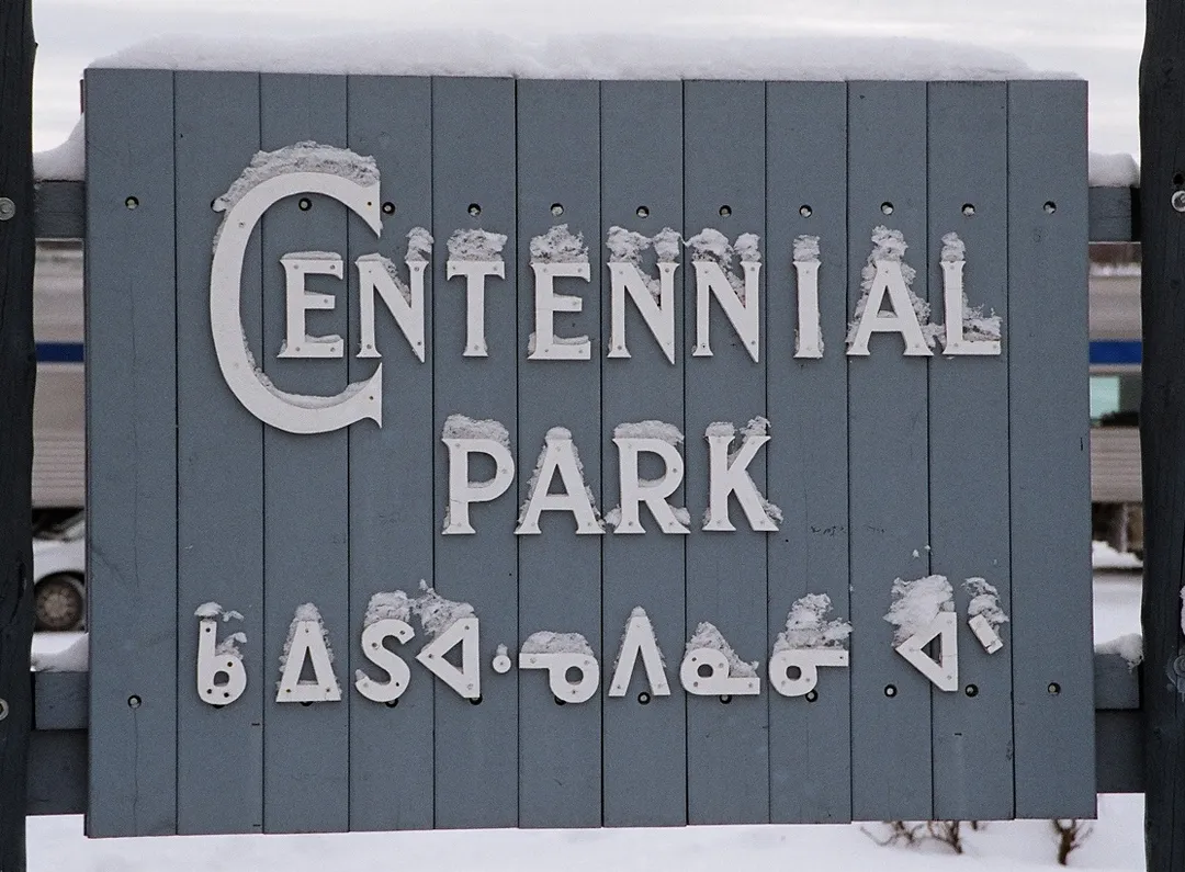 A sign at Centennial Park in Sioux Lookout, Ontario, Canada with Ojibwe Syllabics.
Text: Centennial Park ᑲᐃᔑᐊᓉᐱᓇᓂᐧᐊᐠ

Non-roman text transliteration and translation: fully pointed as ᑳᐃᔑᐊᓉᐱᓈᓂᐗᐣᐠ (Gaa-izhi-anwebinaaniwang); unpointed as ᑲᐃᔑᐊᓉᐱᓇᓂᐧᐊᐠ; translated as "the place where people repose." The second ᐧ (w) is missing from the sign.