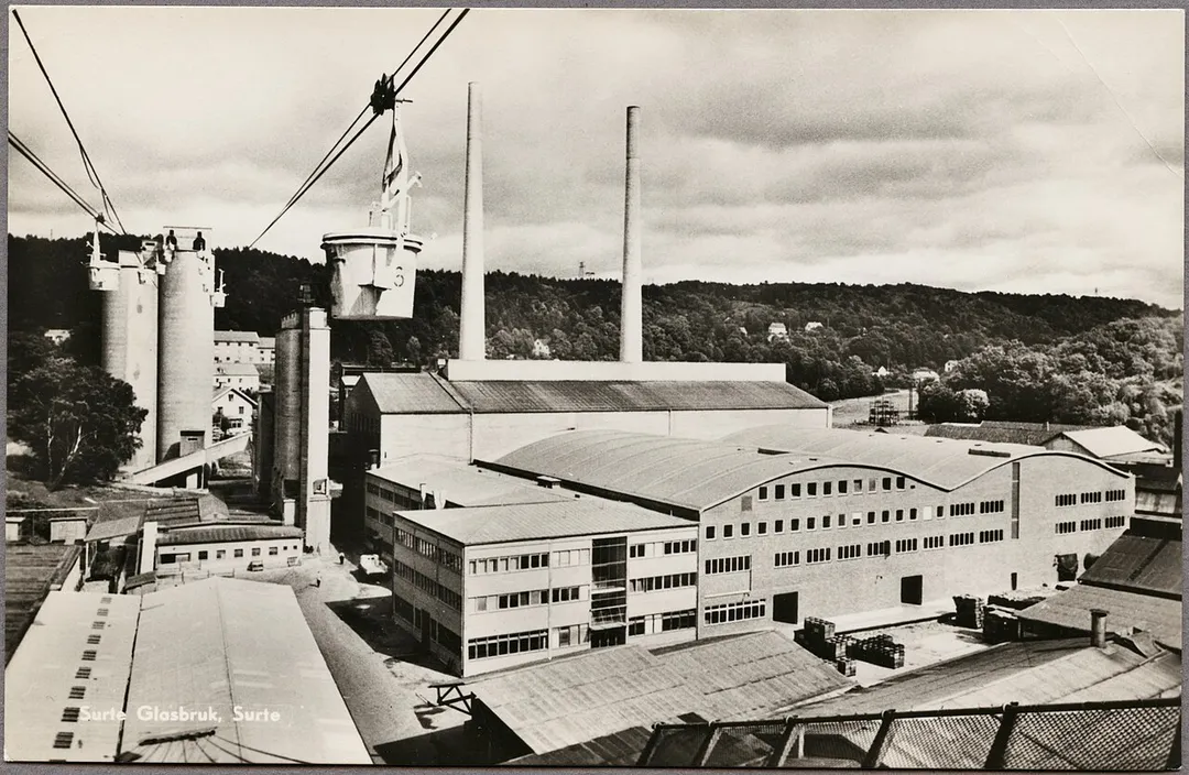 Text på baksida: "Sedan snart 100 år tillverkas glasemballage i Surte vid Götaälvstranden, 15 km norr om Göteborg. Surte Glasbruk är Nordens största och därtill ett av världens modernaste emballageglasbruk. Årsproduktion är c:a 160.000.000 enheter, vilket betyder att 17 järnvägsvagnar med glas varje dag på året lämnar Surte.".