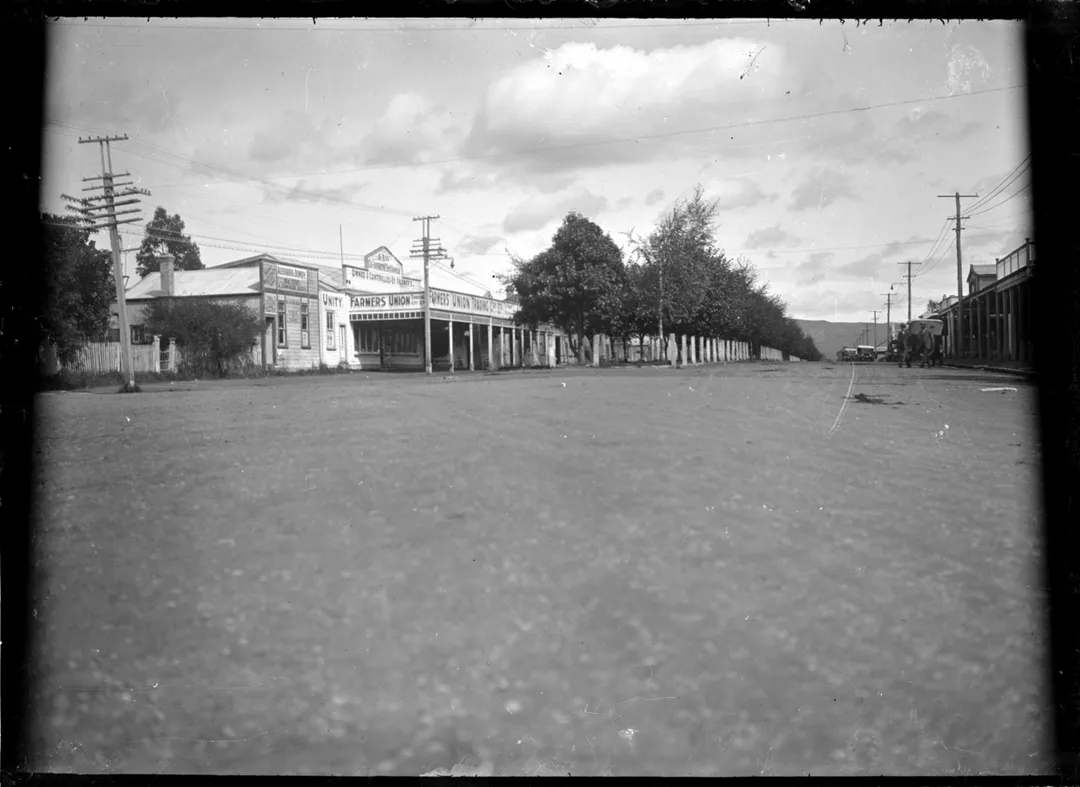 View of the Main Street in Te Puke in 1924. The premises of Alexander &amp; Dowdy,  real estate agents, and the Farmers' Union Trading Company are visible centre left. Photographed by Albert Percy Godber. Dated from other images in Godber Album Vol 109.