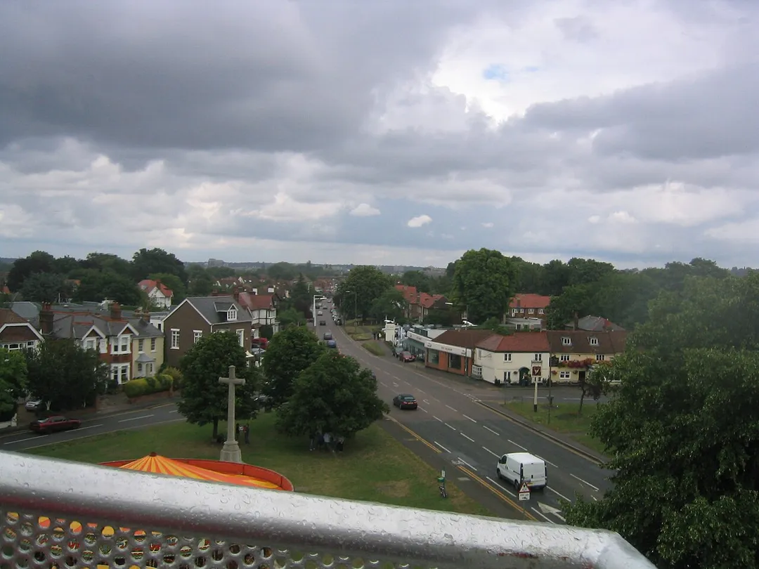 Slight rise in road of 'Giggs Hill' or Giggs Hill Green, a village green in Thames Ditton, showing the distant slopes of Richmond Park on the horizon, including Kingston Hill. Taken by the contributor, Summer 2005.  The main road has a bypass. It is part of the London-Surrey Classic event in August in cycling.