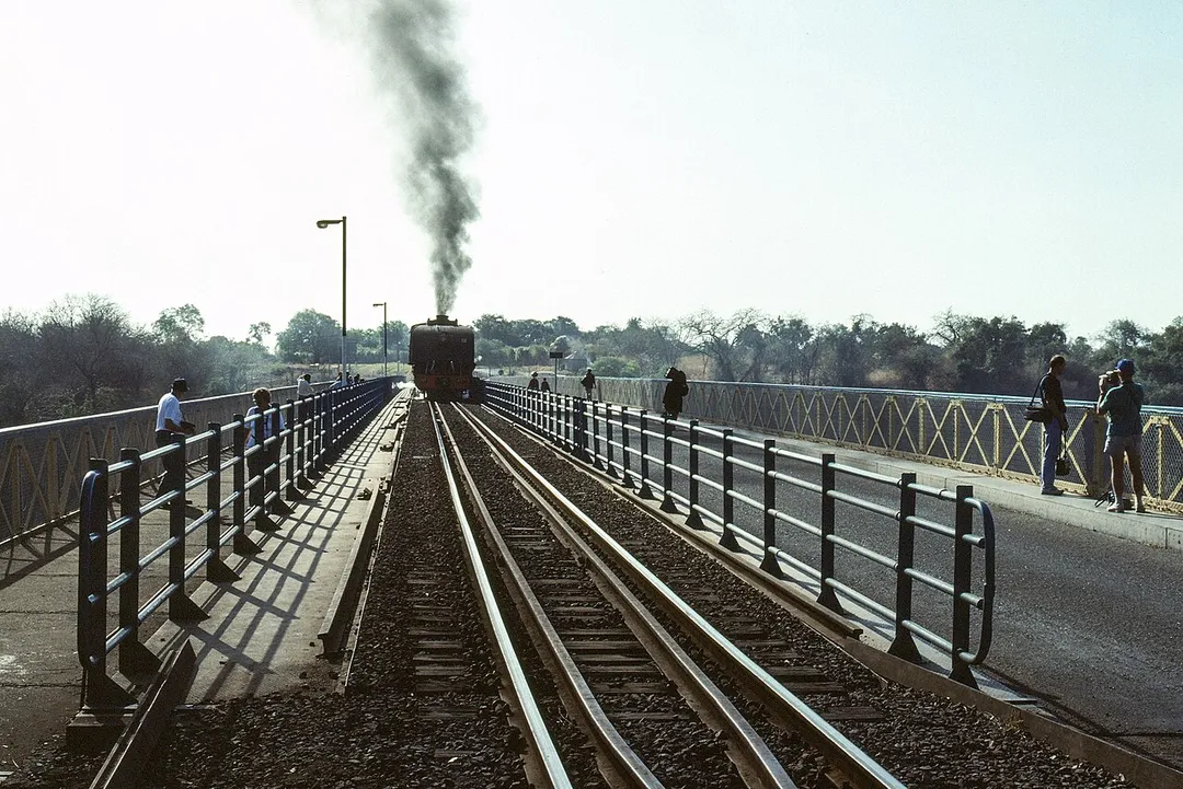 National Railways of Zimbabwe 15A class 4-6-4+4-6-4 'Garratt' locomotive no. 407 'Ukhozi' ('Eagle', built by Beyer Peacock in 1950) has been positioned for photographic purposes with a short train on Victoria Falls bridge for a couple of hours.

A small fee bought a pass to walk onto the bridge, which can be seen to also have a road and a footpath.  Victoria Falls town in Zimbabwe is behind the train which is facing towards Zambia, the Zambezi River is below, and Victoria Falls is away to the right.  There was a steady stream of vehicles and pedestrians across the bridge, and a few trains (when this train was not there!).