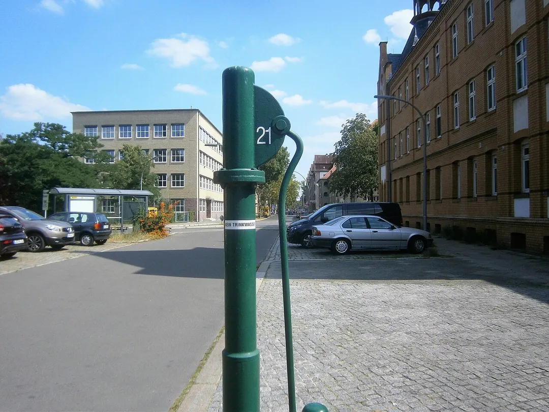 Auf dem gelisteten Grundstück Adamstraße 24 (Drucksache zur Anfrage 17-15418) steht das Gebäude der Paul-Mohr-Schule[1] und das Grundstück liegt östlich vom Melanchthonplatz.[2] Der Schulbau entstand 1930. Für eine Umsetzung des Brunnens gibt es keine Anzeichen. Der Standort des Brunnens liegt am Norden des Melachthonplatzes am Gehwegrand des Parkplatzes der die Adamstraße verlängert. Der Bogen in der  Straßenführung erfolgte in den 1960er Jahren, zuvor verlief die Adamstraße im Süden der Melanchthonkirche gerade und die Melanchthonstraße kreuzte rechtwinkling mit dem Verlauf auf dem Westen des Schulgeländes. Die direkte Führung über die Wilhelmstraße zur Schmidt-Knobelsdorf-Straße erfolgte unter Nutzung der Kolonie Diederich. Dadurch wurde der Melchthonplatz mit dem Kirchenbau neu gefasst. Gegenüber der Kirche auf der Brunnenseite steht ein Seniorenwohnhaus[3] Der Brunnenstandort entspricht dem Rand des südlichen Gehwegs. Deer Austritt ist an einer langen Hülse verschraubt und der Abfluss gelangt auf die Gehwegplatten zwischen Parkfläche und Ausfahrt vom Heim. Der FSH-Brunnen steht mindestens seit Beginn der 2000er Jahre.